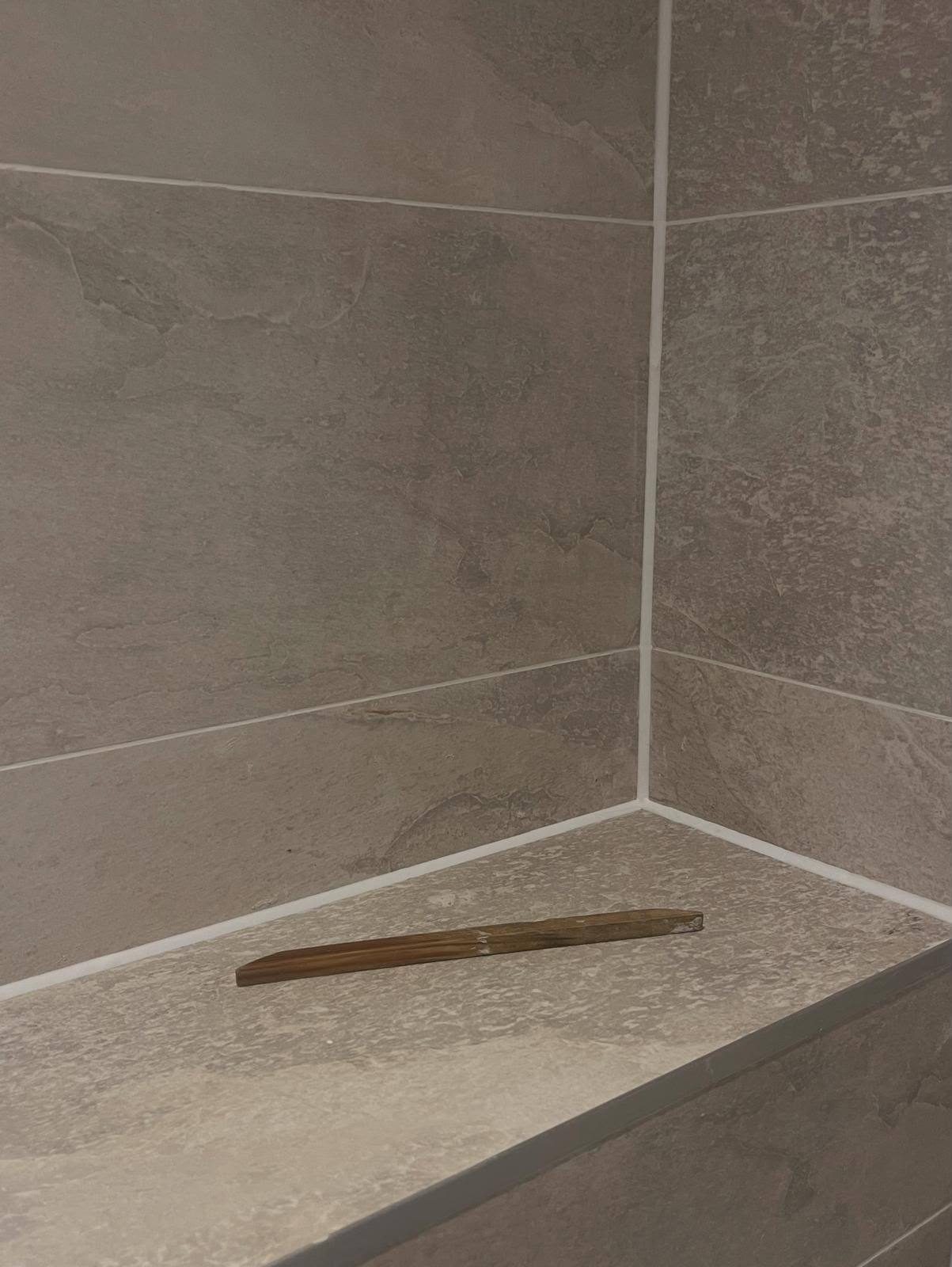 Freshly replaced white silicone sealant in a grey stone-tiled shower corner and seat