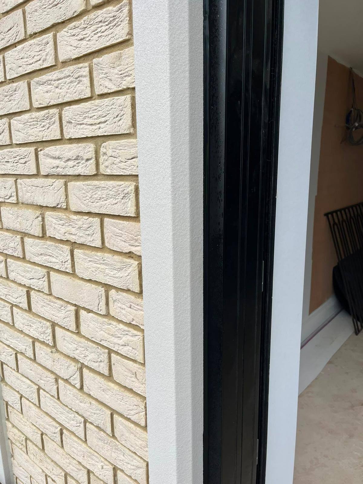 Textured white external sealant joint between a black door frame and brickwork