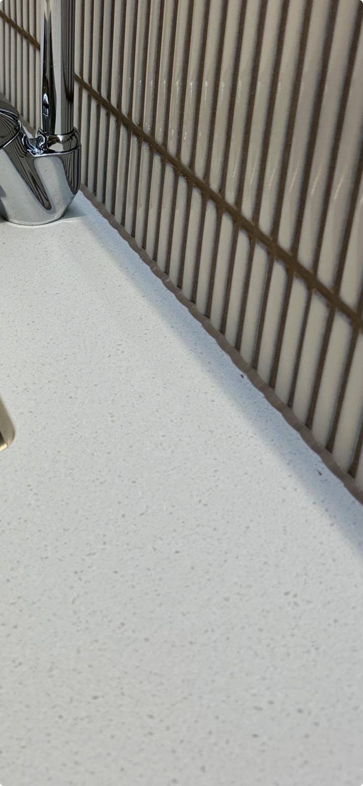 Chrome tap and worktop sealed to vertical beige splashback tiles
