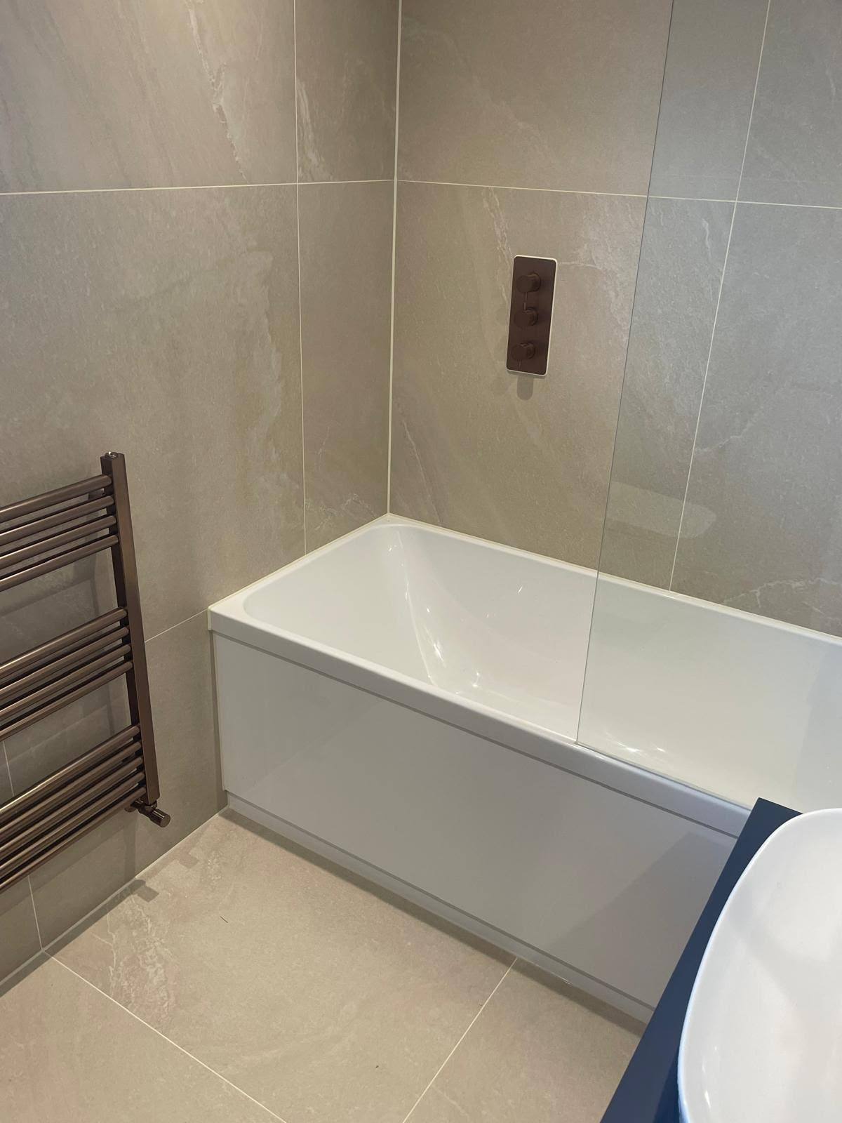 White bath silicone sealed to tiled walling beside a glass shower screen