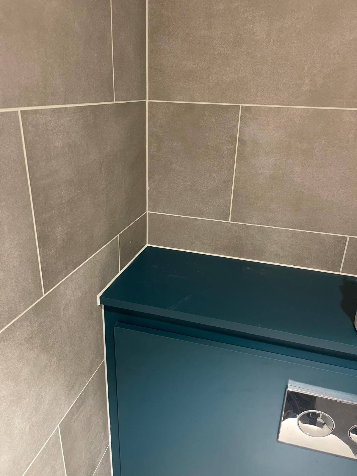 White silicone bead where a teal bathroom cabinet meets grey tiling