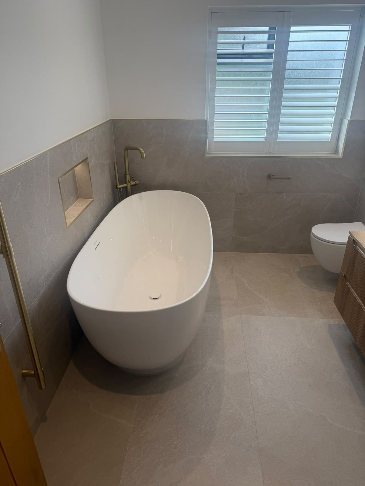 Freestanding bath in a grey stone-tiled bathroom with crisp silicone sealing to wall and floor joints