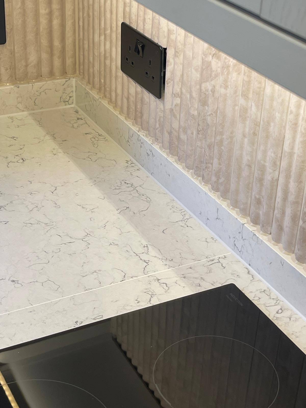Crisp white sealant line where a marble worktop meets a fluted splashback