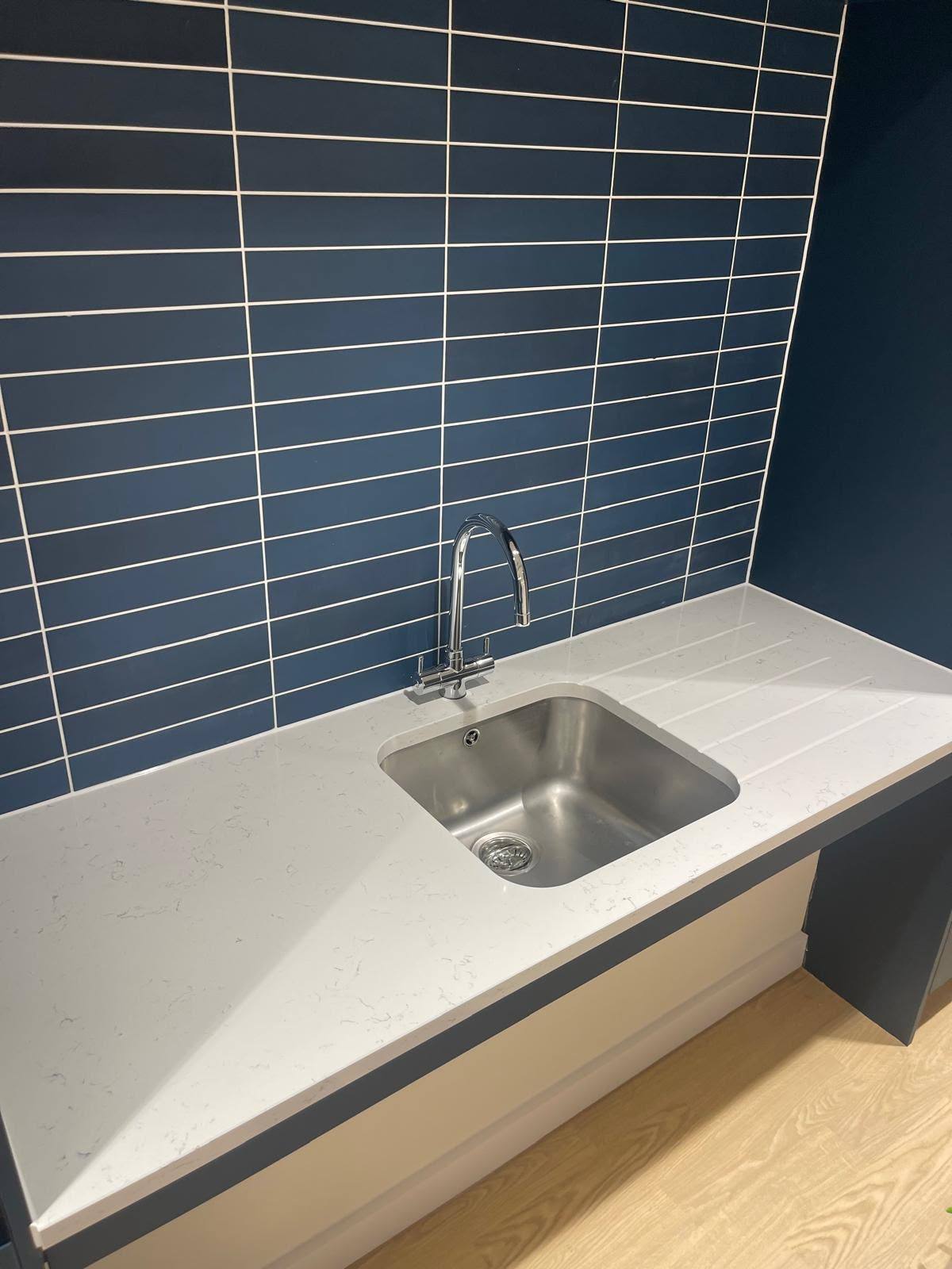 Stainless steel sink sealed into a marble worktop against blue tiling