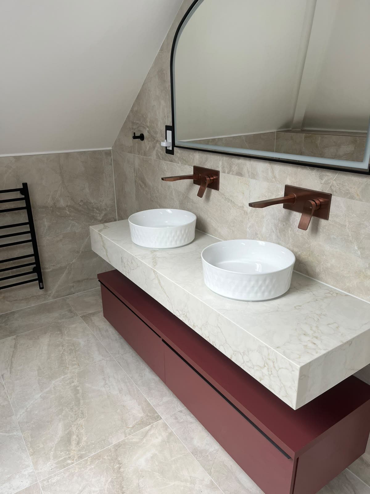 Double vessel basins on a stone worktop sealed to tiled wall above a burgundy vanity