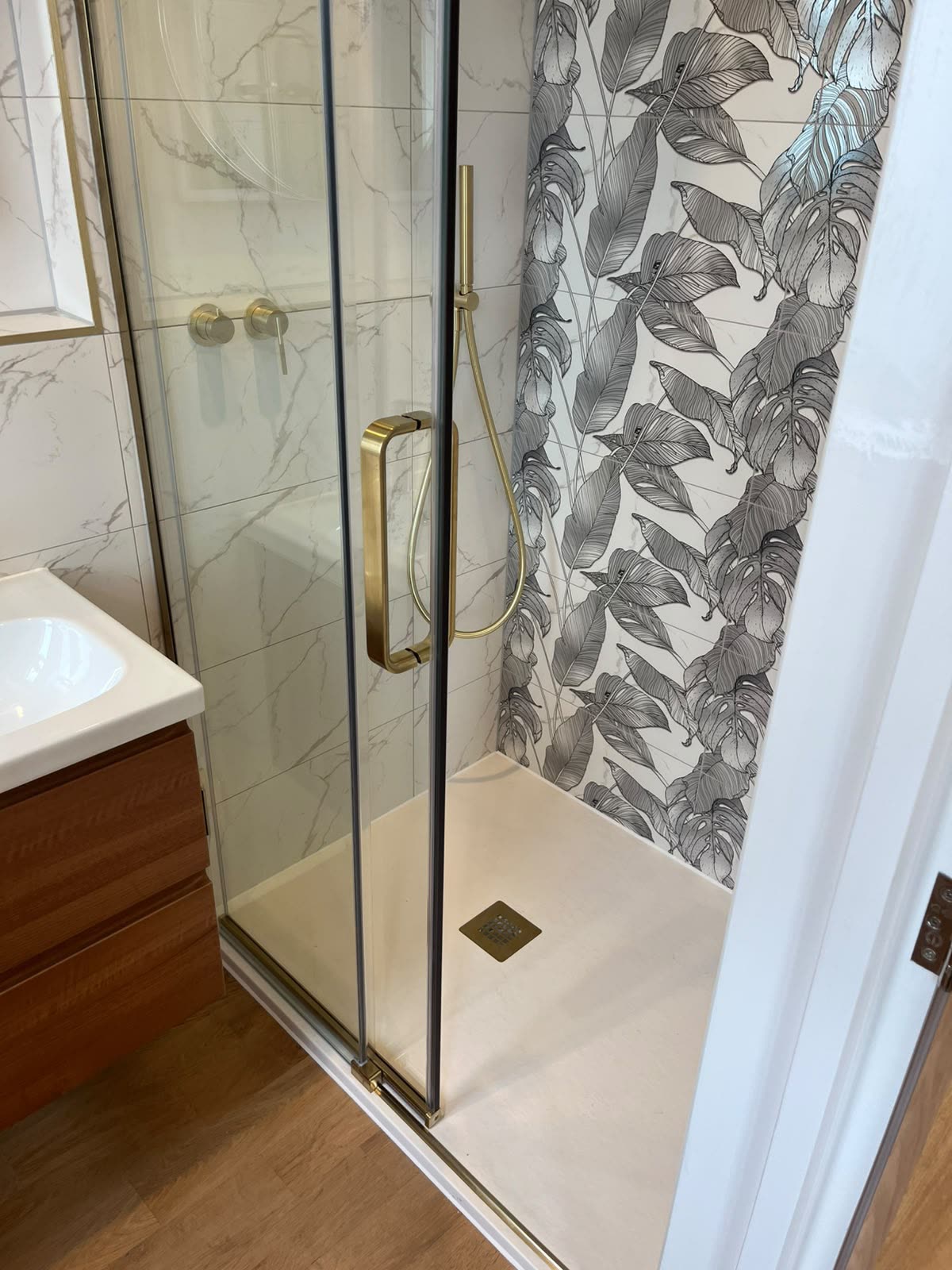 Shower enclosure with botanical feature tiles and a stone tray sealed with white silicone