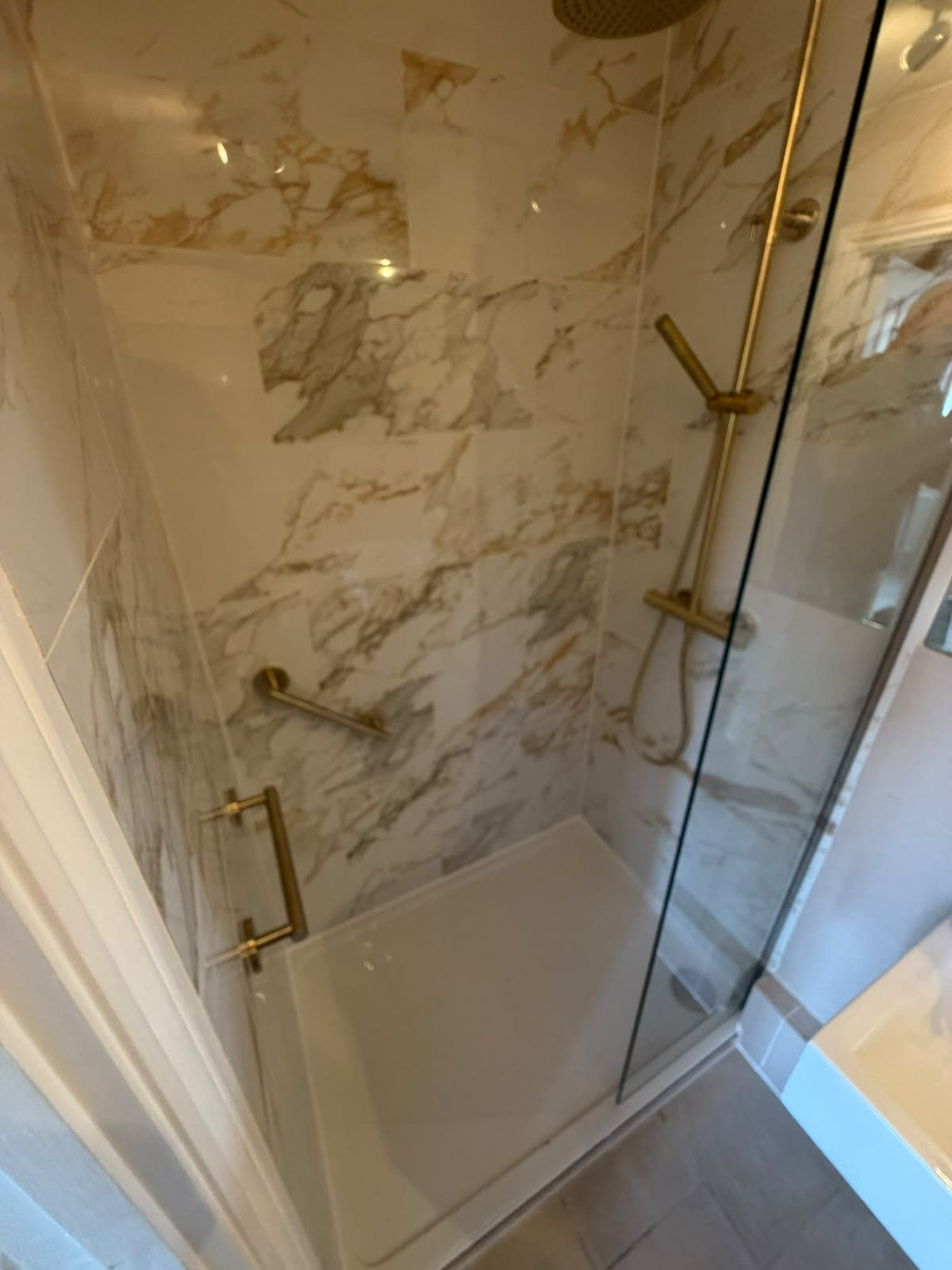 Marble-effect shower with brass fittings and shower tray sealed to wall tiles