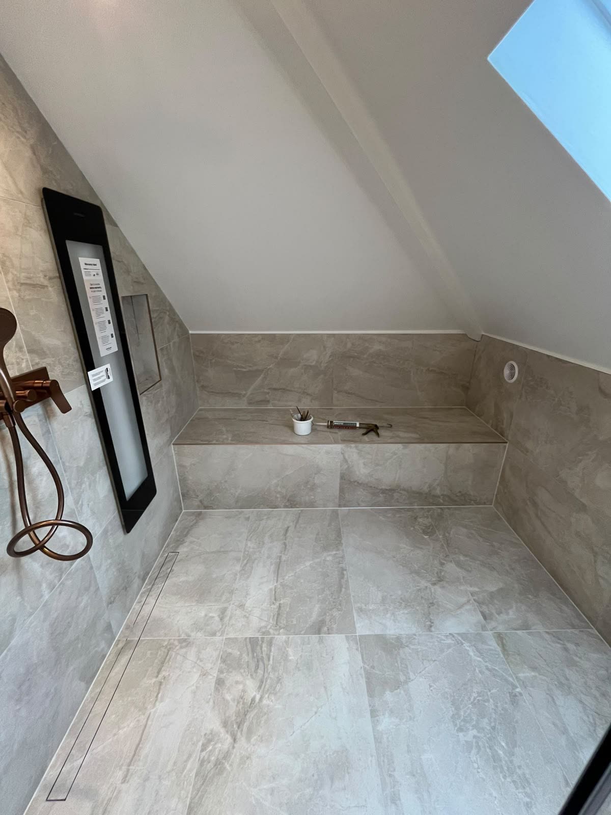 Loft wet room with tiled bench and floor joints freshly silicone sealed, sealant gun on the bench